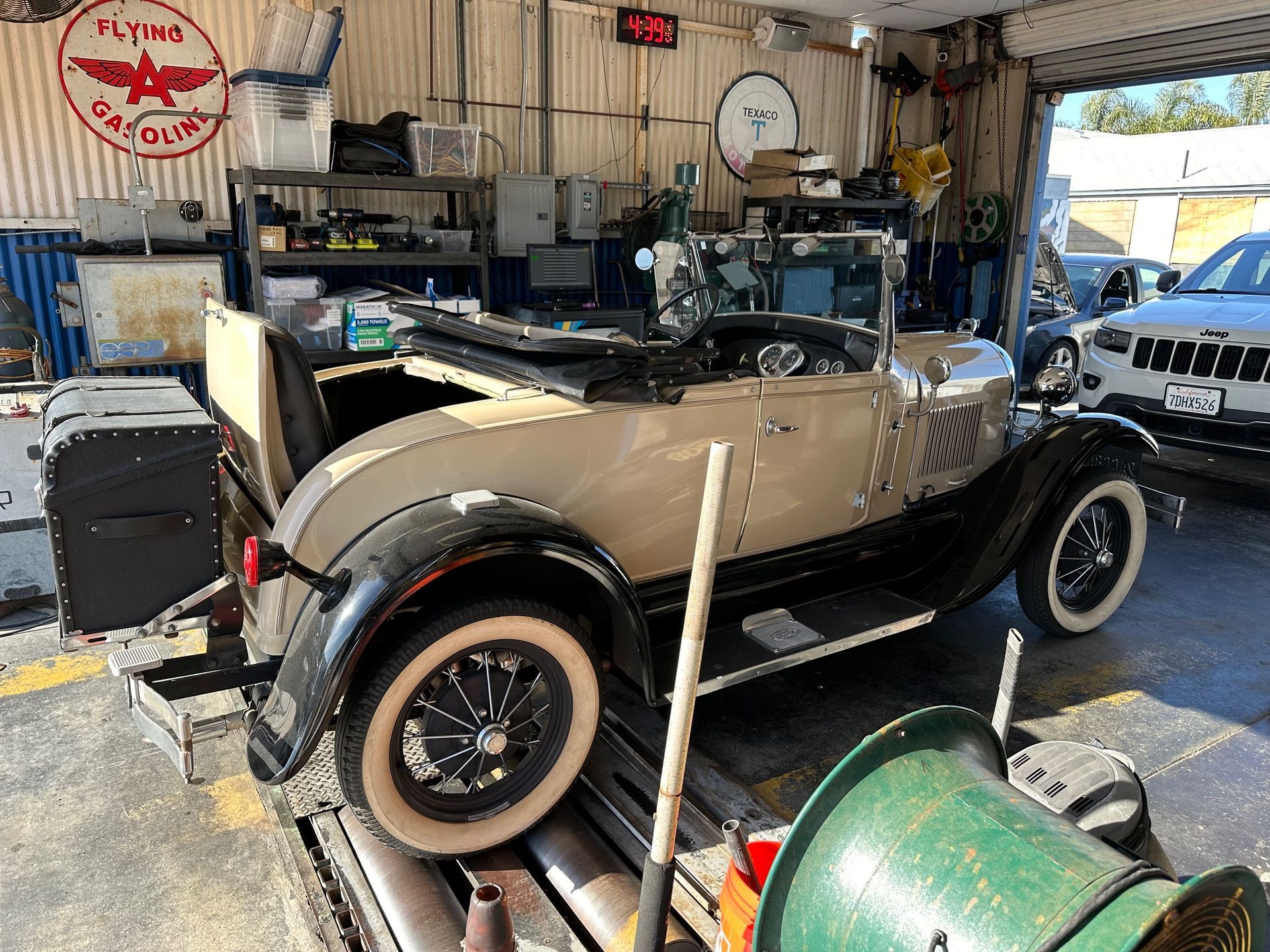 Vintage beige convertible in a cluttered garage, with whitewall tires and workbenches in the background