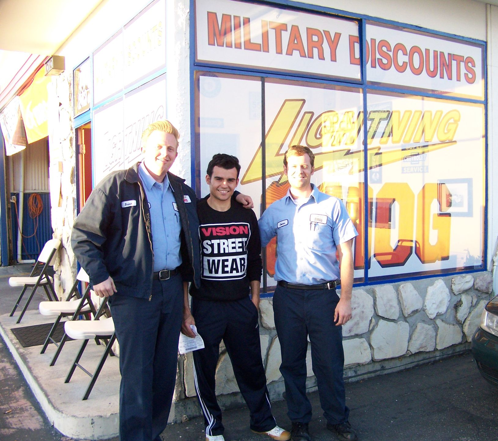 Three men stand outside a storefront with "Military Discounts" and bright orange sale signs.